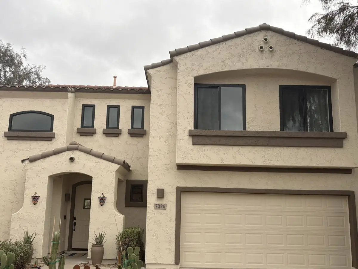 A two-story stucco home with dark frame windows, including a small arched window over the entry