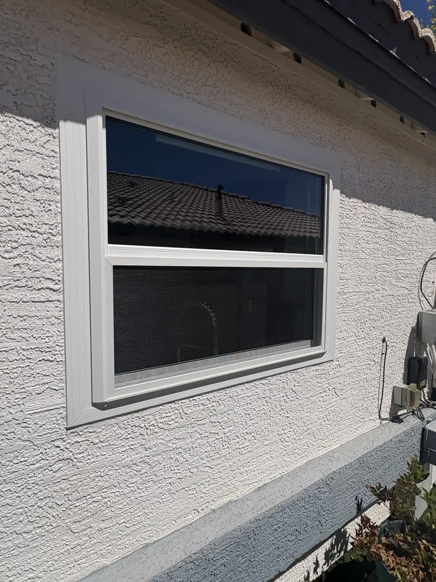 A wide single-hung window in a stucco wall under the roof line